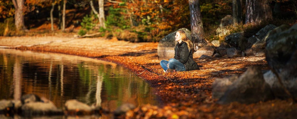 En personer sitter vid en sjö och vilar bland höstlöv